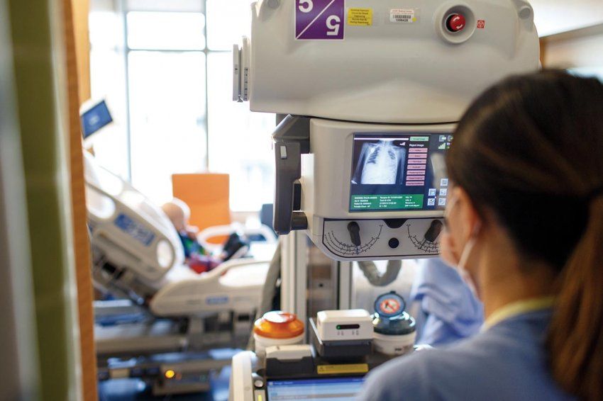 A technician looks at a mobile X-ray machine with a young patient in the background.