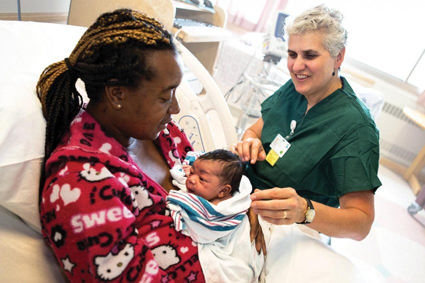 A nurse talks to a mother and her newborn baby in a hospital bed.