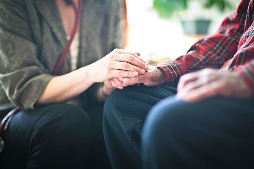 A woman’s hand rest on an elderly person’s hand.