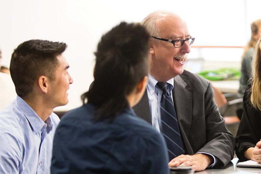 Dean David Vlahov speaking with a group of people around a table.