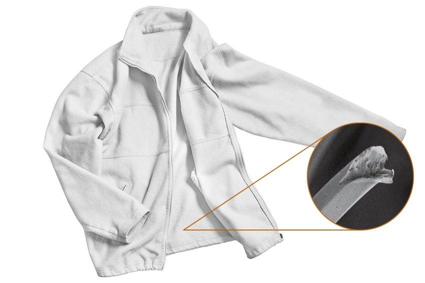 A white fleece jacket with a zoomed-in callout that shows a microscopy image of a polyester fleece fiber that are broken and frayed.